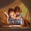Mother and child reading in tent with flashlight, cozy nighttime story session, portable LED light.